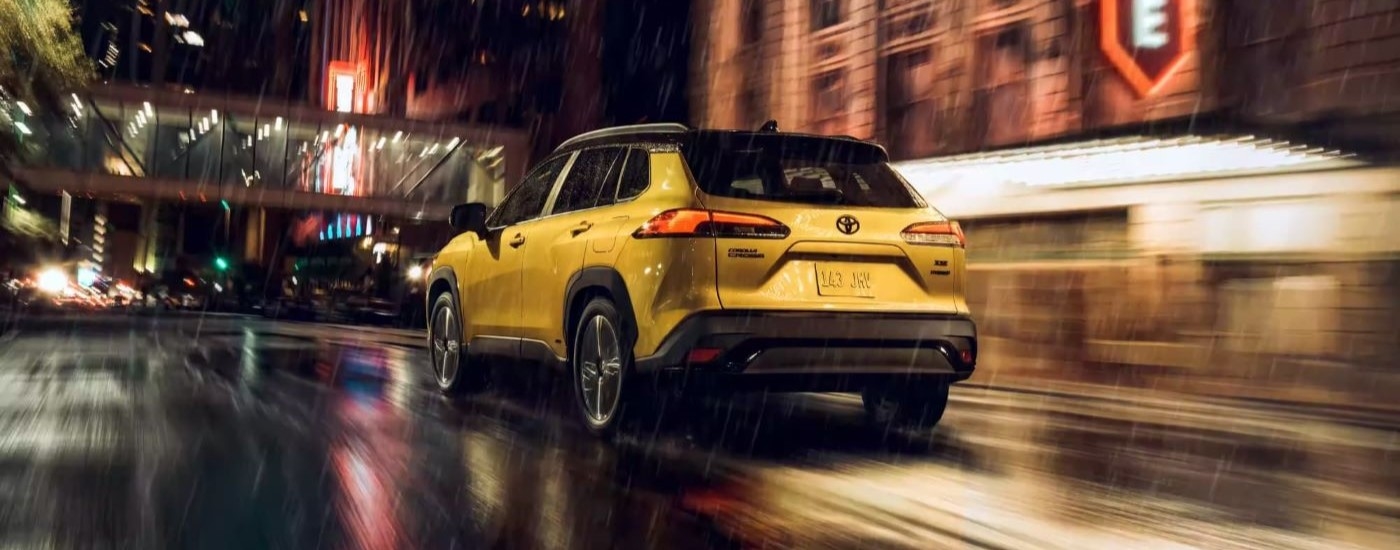 A yellow 2023 Toyota Corolla Cross Hybrid XSE is shown driving on a rainy city street.