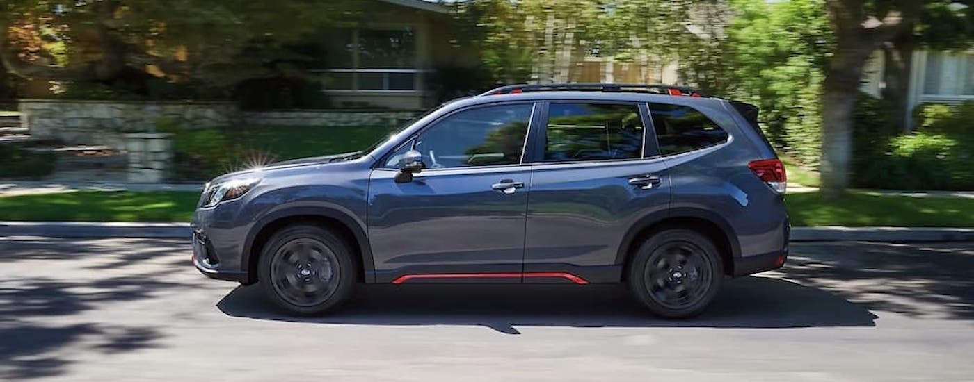 A grey 2024 Subaru Forester is shown from the side on a suburban street.