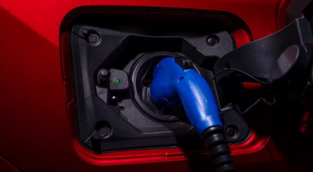 A close up shows a blue plug charging a red 2023 Toyota RAV4 Prime.