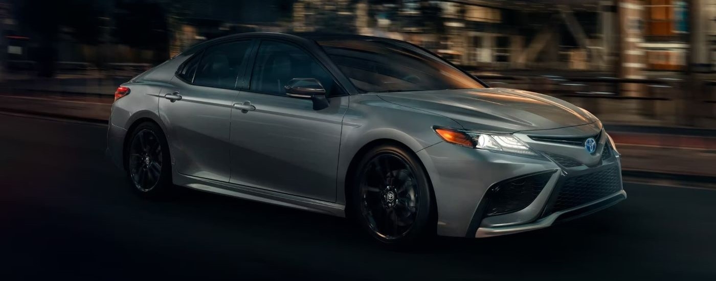 A silver 2024 Toyota Camry XSE Hybrid is shown on a city street at night.