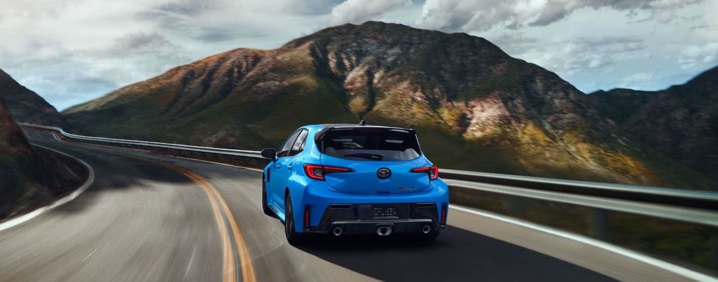 A blue 2024 Toyota GR Corolla is shown from the rear on a mountain road.
