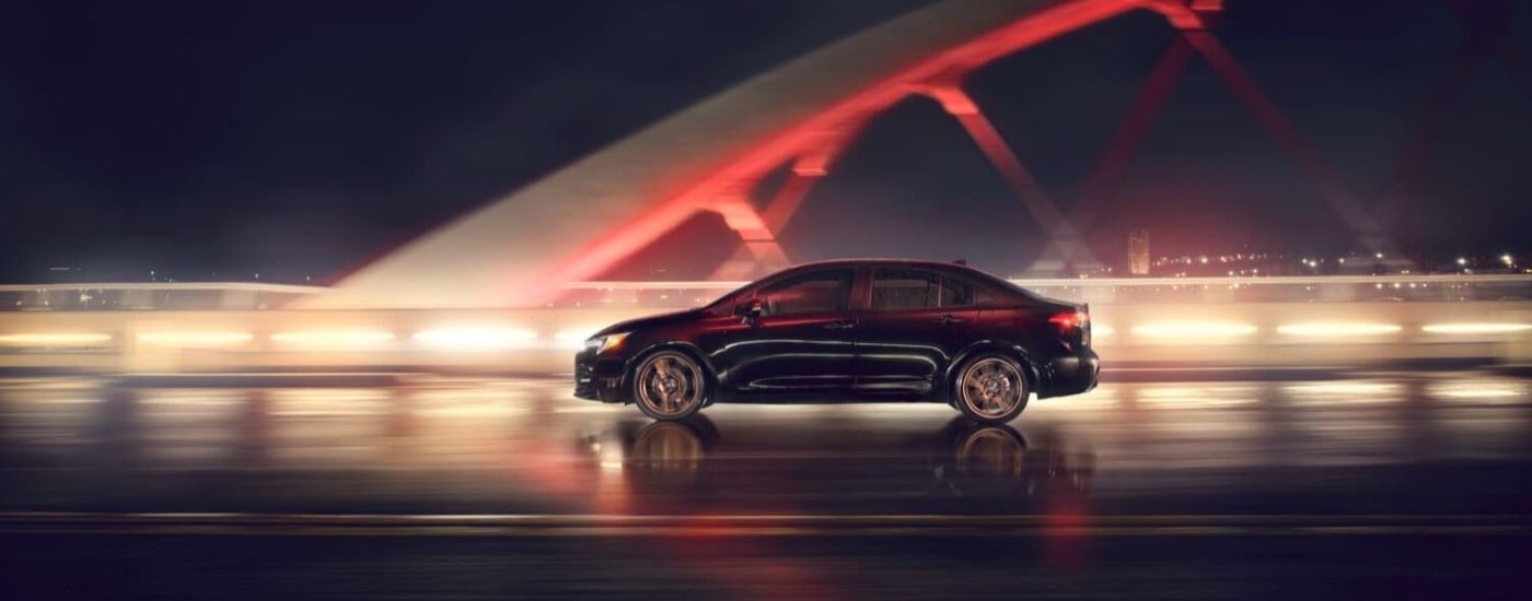 A black 2024 Toyota Corolla Nightshade is shown from the side driving over a bridge at night.