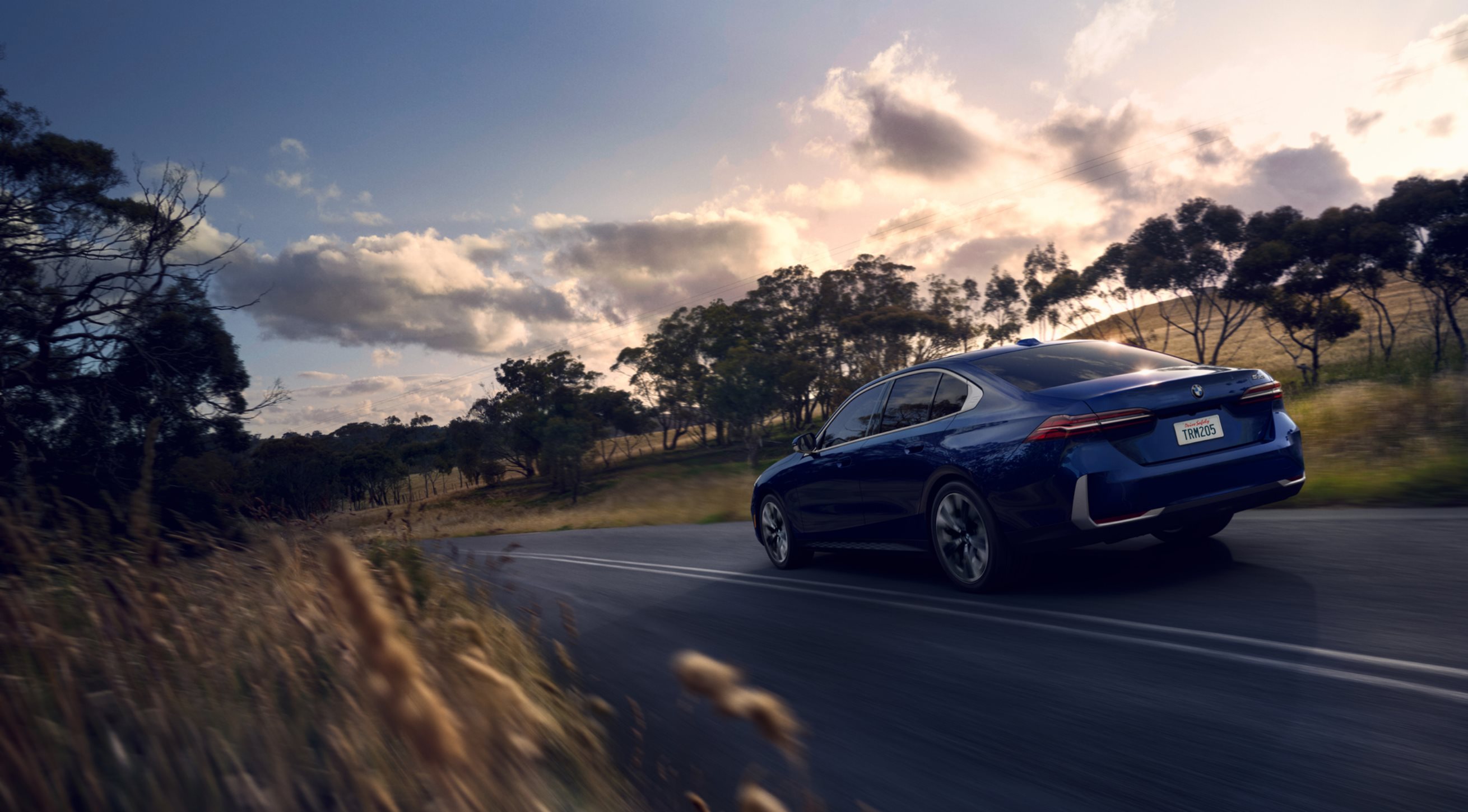 2024 BMW 5 series in blue cruising down a country road.