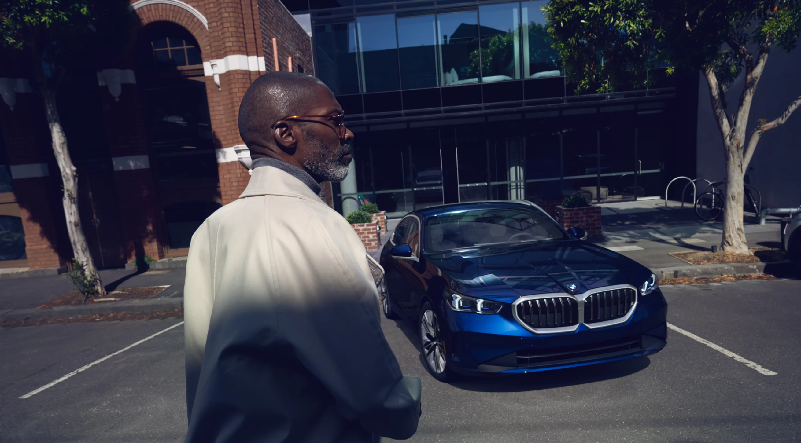 2024 BMW 5 Series in blue parked in front of building with man in foreground.