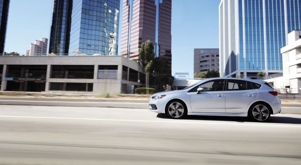 A silver 2021 Subaru Impreza is shown from the side driving on a city street.