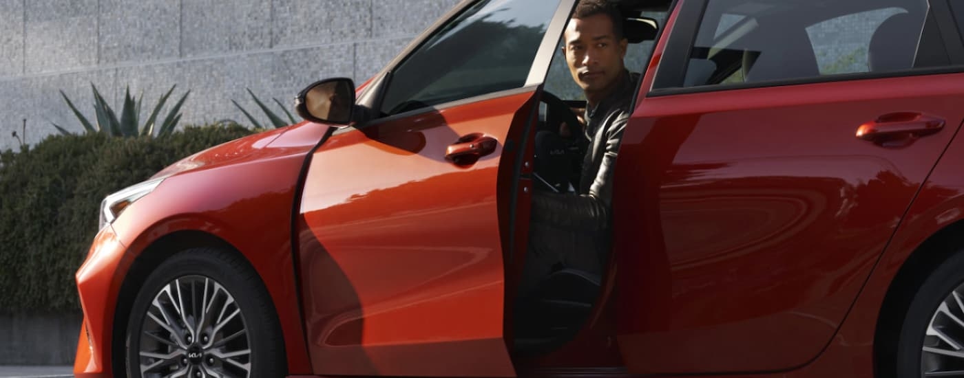 A man is shown getting out of the driver's side of an orange 2023 Kia Forte.