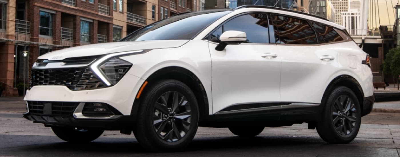 A white 2023 Kia Sportage Hybrid is shown driving on a city street after leaving a used Kia dealer near Corpus Christi.