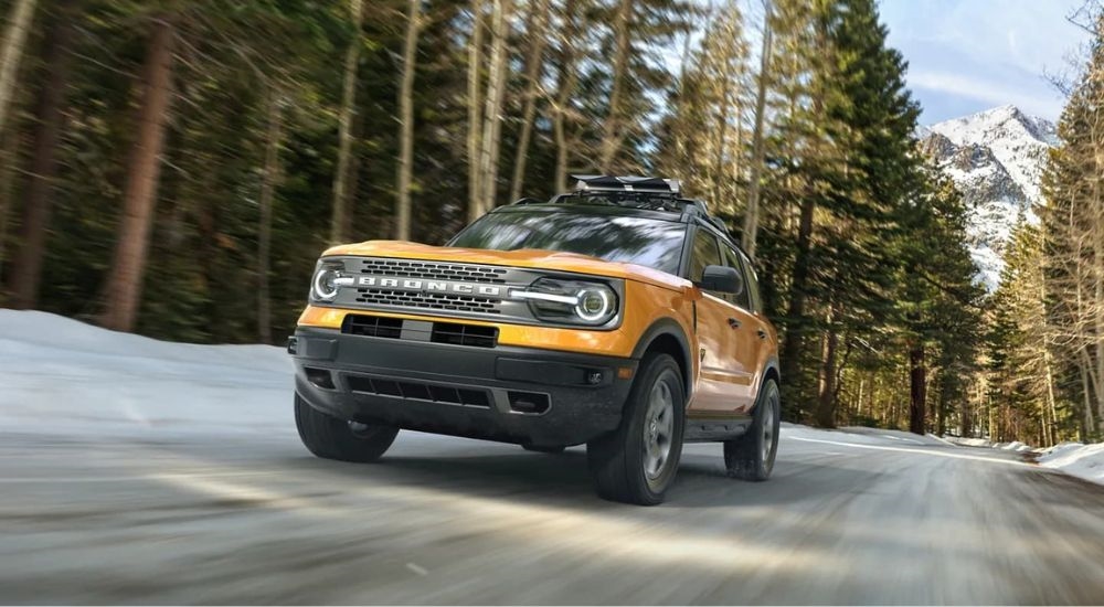 A yellow 2023 Ford Bronco Sport for sale is shown driving on a snowy road.