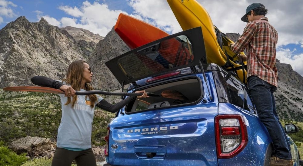 People are shown stowing kayak equipment in the back of a blue 2024 Ford Bronco Sport.