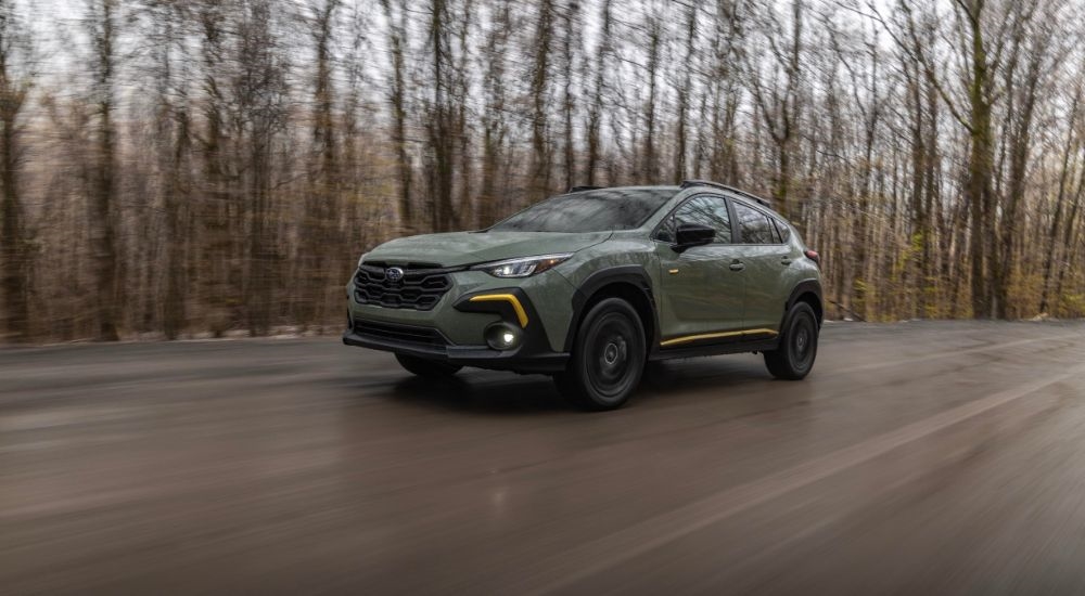 A green 2024 Subaru Crosstrek Sport is shown driving on a wet road.