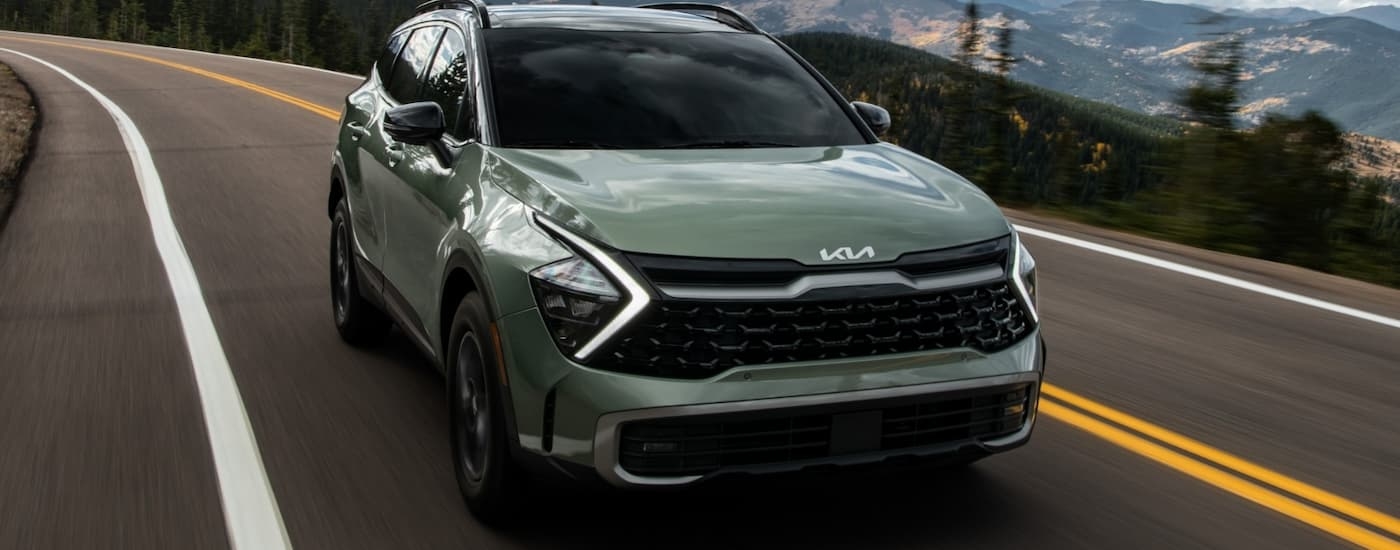 A green 2024 Kia Sportage is driving on an open road.