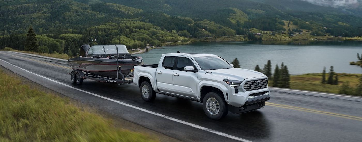 A silver 2024 Toyota Tacoma for sale is shown from the front at an angle while towing a boat.