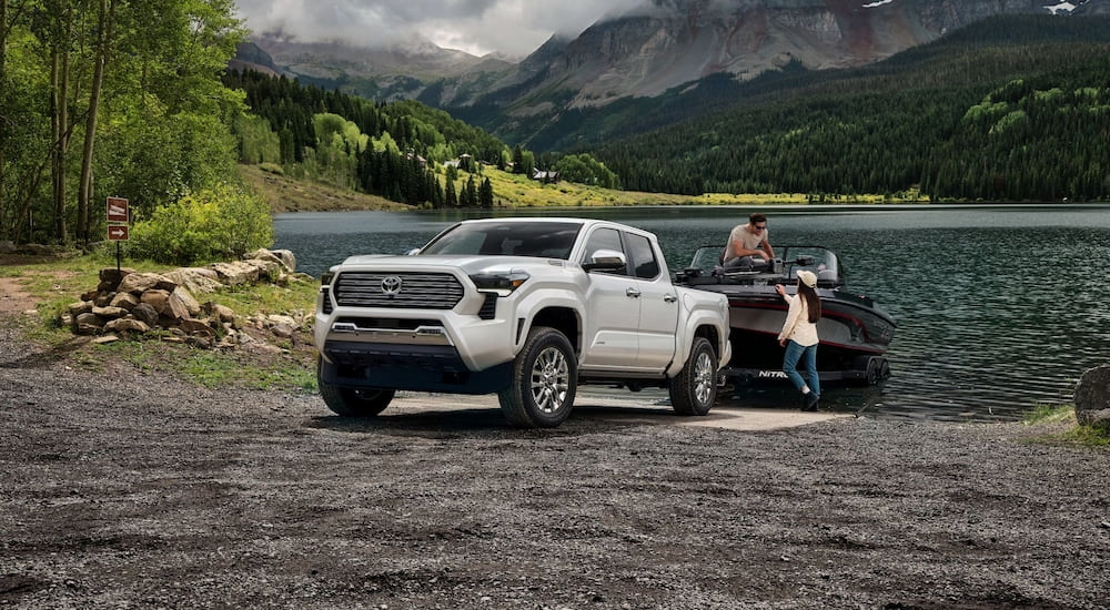 A white 2024 Toyota Tacoma Limited is towing a boat out of a lake.