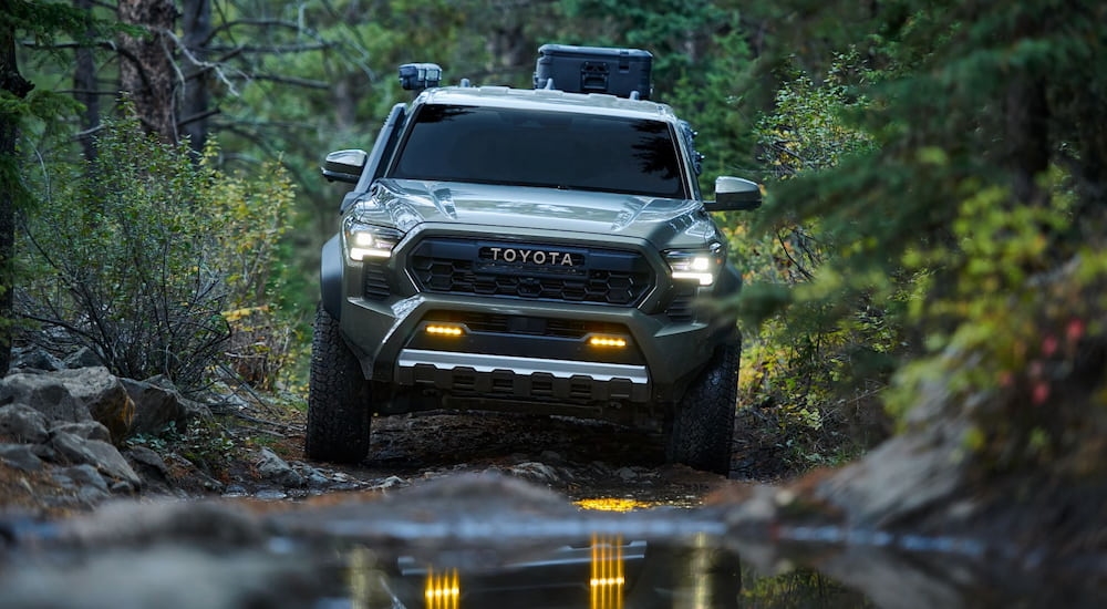 A green 2024 Toyota Tacoma Trailhunter is about to drive through a muddy puddle on a trail.