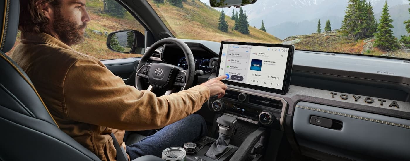 A man is using the infotainment screen in a 2024 Toyota Tacoma.
