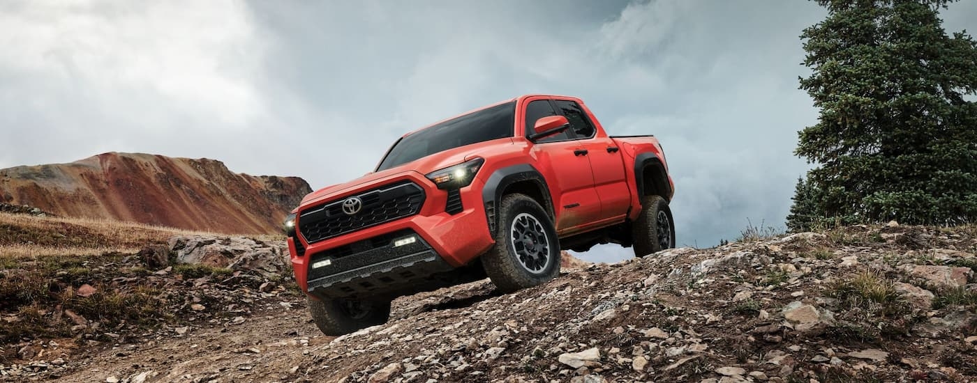 A red 2024 Toyota Tacoma TRD Off-Road is driving on a rocky dirt road.
