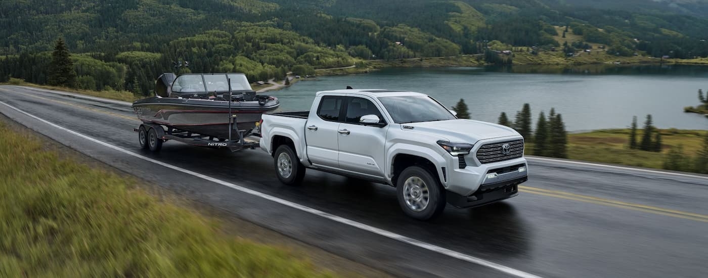 A white 2024 Toyota Tacoma is towing a boat on an open road.
