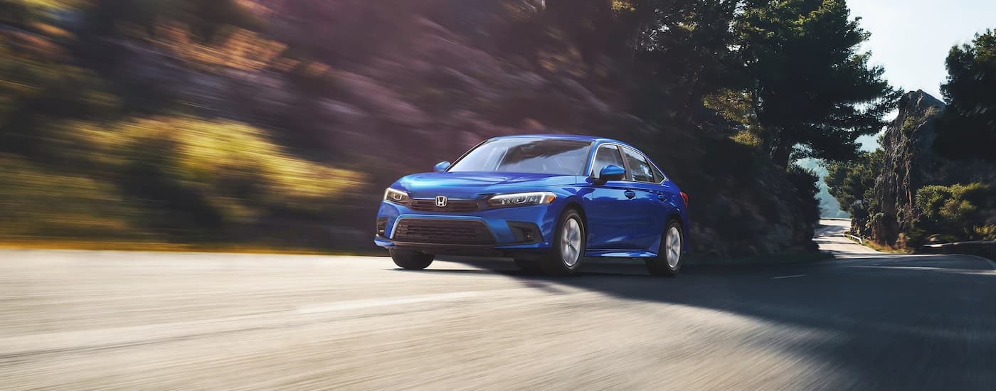 A blue 2022 Honda Civic LX is shown driving on an open road lined with trees.