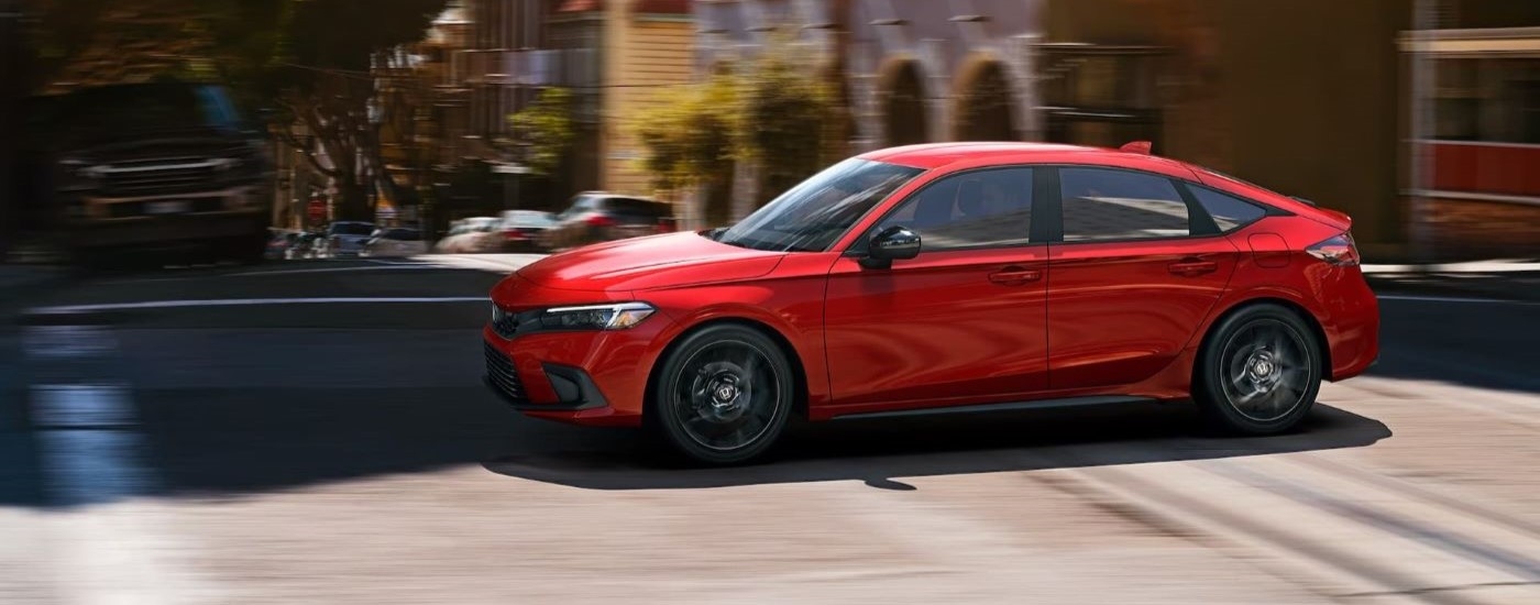 A red 2022 Honda Civic Hatchback driving on a city street after leaving a used car dealership.