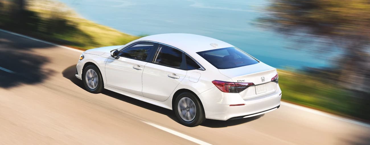 A white 2022 Honda Civic driving on an open road with a view of a lake.