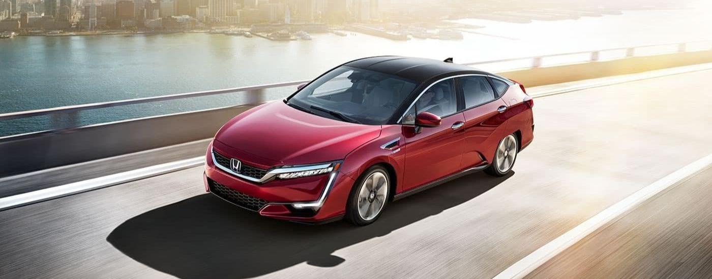 A red 2017 Honda Clarity Fuel Cell EX is shown driving past a used car dealership near North Bergen.