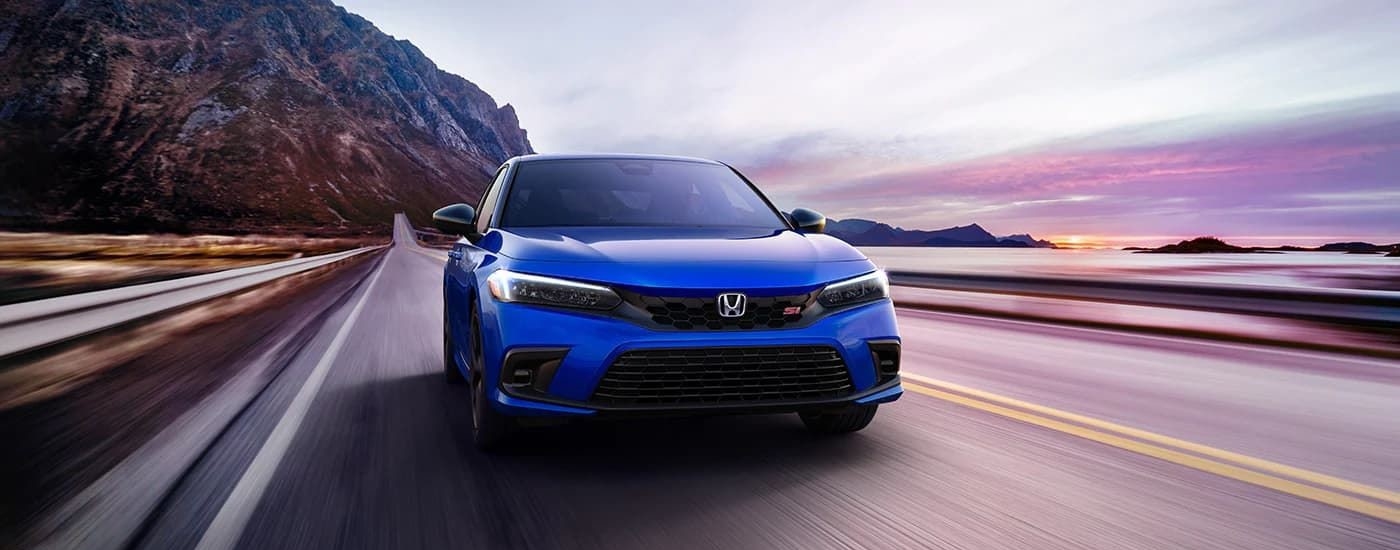 A blue 2023 Honda Civic Si is shown driving at sunrise.