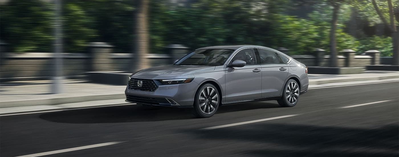 A grey 2023 Honda Accord Touring driving past a city park.