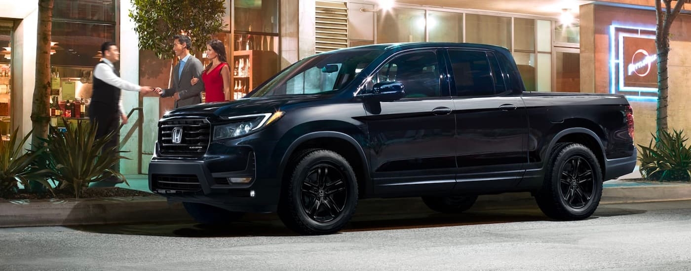 A black 2023 Honda Ridgeline Black Edition parked on a city street in front of an upscale restaurant.