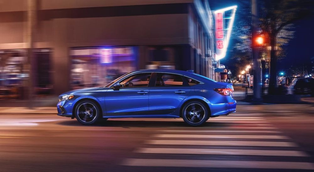 A blue 2024 Honda Civic Touring is shown from the side driving on a city street at night.