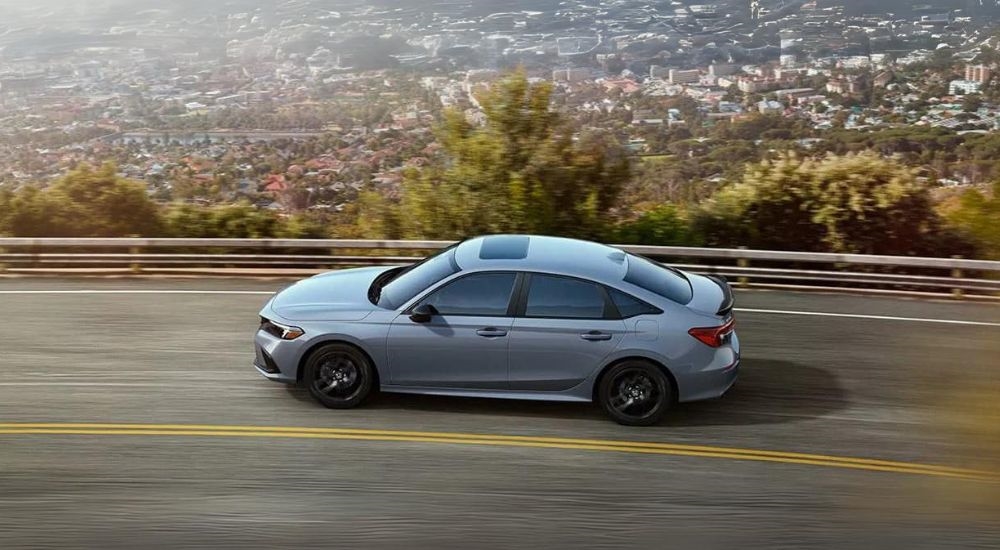 A grey 2022 Honda Civic Si driving on a highway overlooking the city.