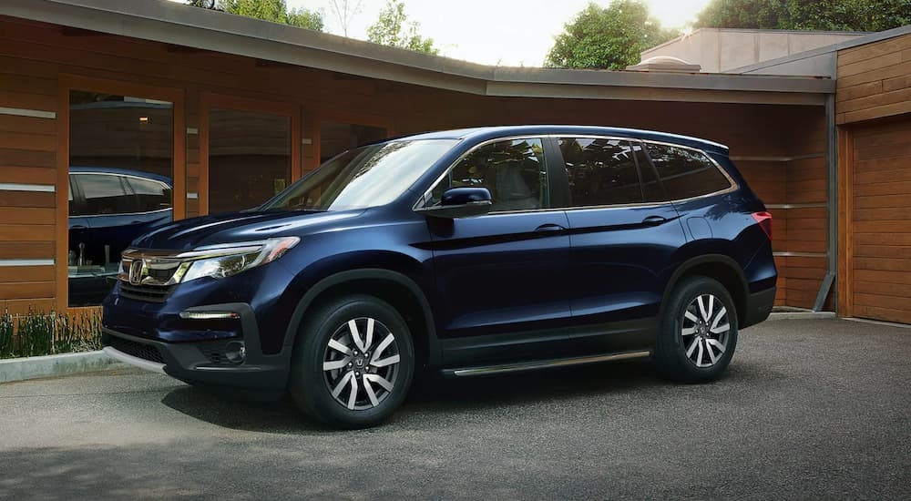 A blue 2022 Honda Pilot parked in front of a modern home.