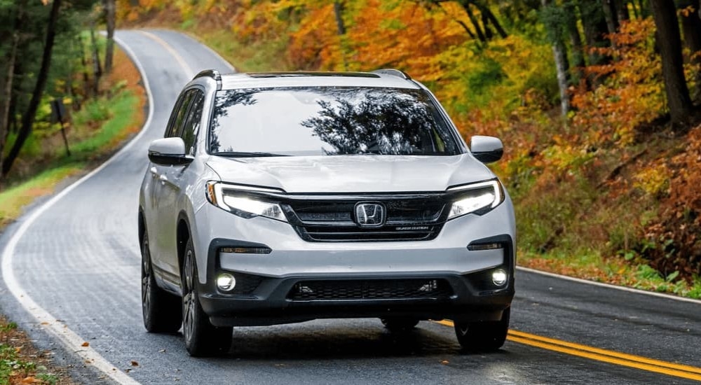 A white 2022 Honda Pilot driving on a winding road to a used car dealership in Union City.