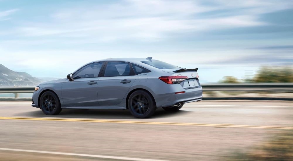 A grey 2023 Honda Civic Si is shown from the side driving on a highway.