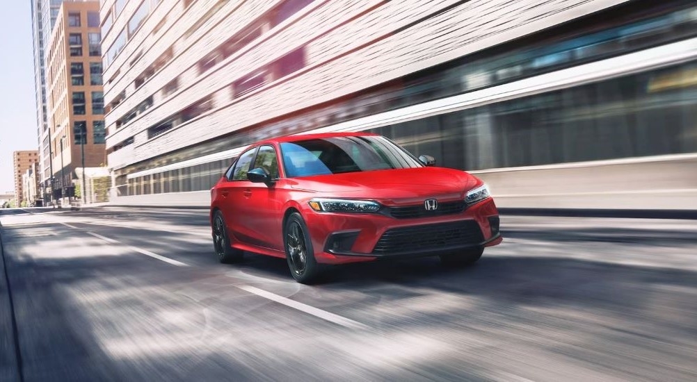 A red 2023 Honda Civic Sport driving through the city.