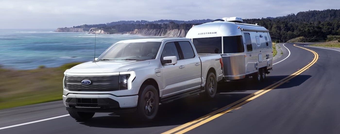 A white 2022 Ford F-150 Lightning is shown towing a trailer on a highway.