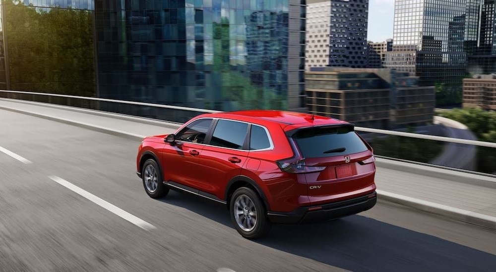 A red 2024 Honda CR-V for sale is driving on a city street.