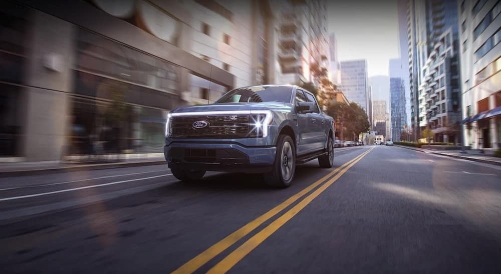 A blue 2024 Ford F-150 Lightning for sale is shown driving on a city street.