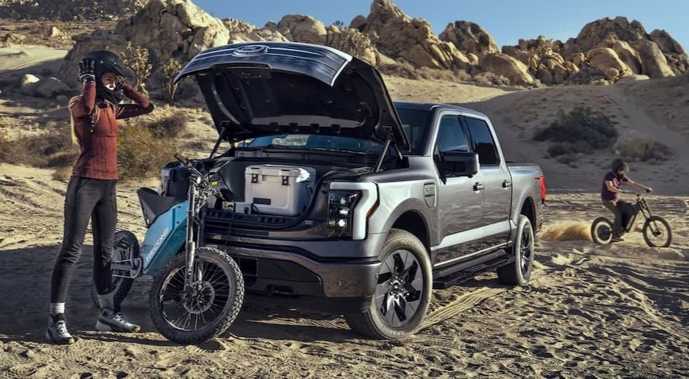 A silver 2024 Ford F-150 is shown parked near two people and their dirt bikes.