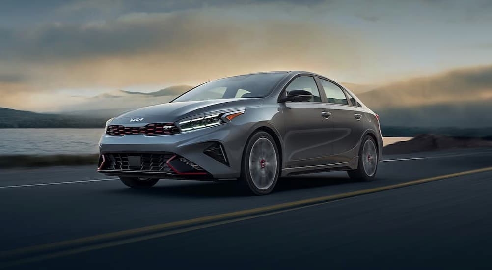 A gray 2024 Kia Forte GT is shown driving near a lake.