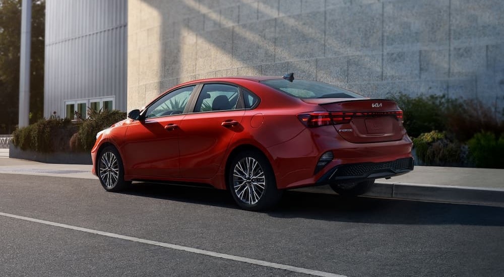 A red 2024 Kia Forte for sale near Bloomington is shown driving on a city street.