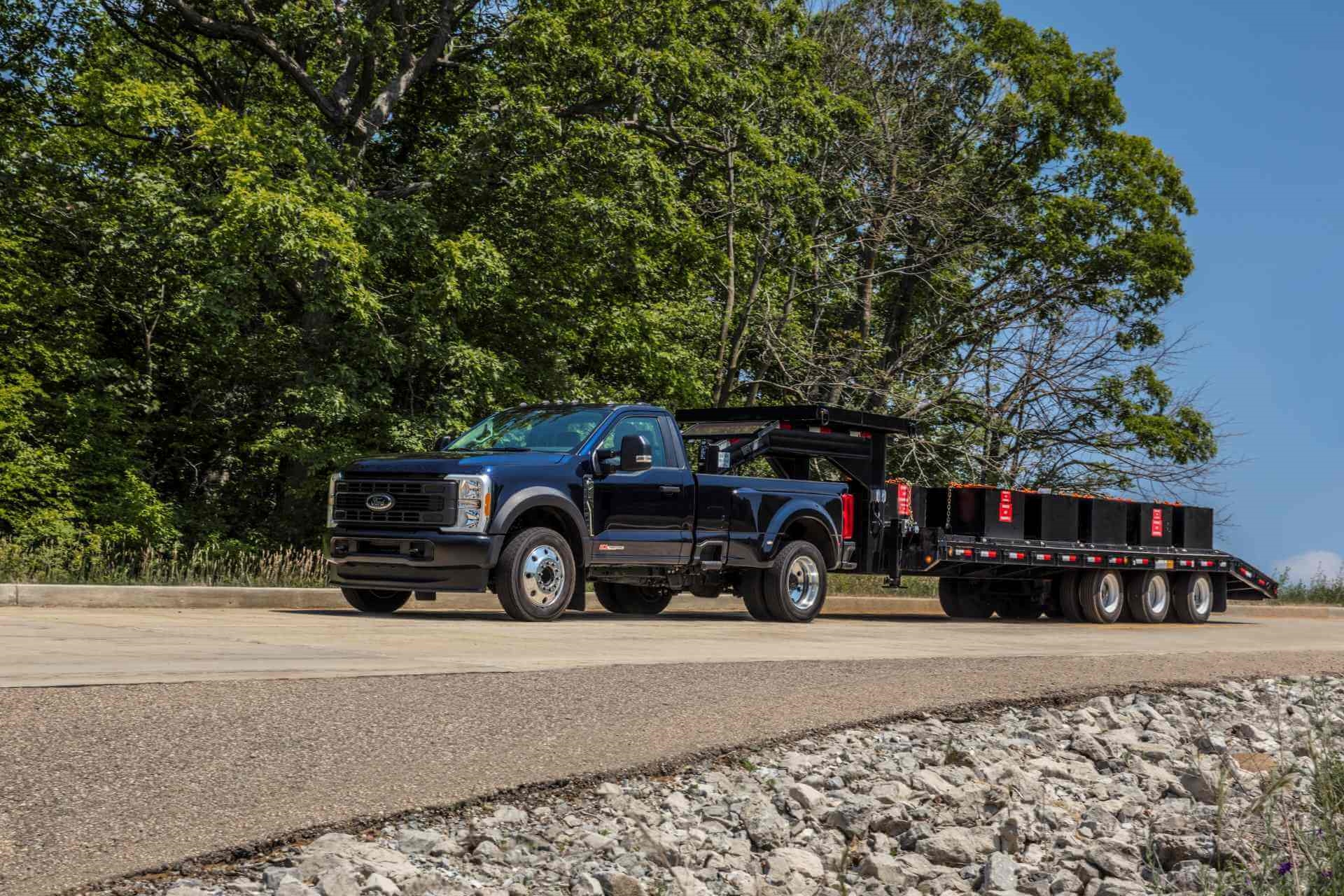 Ford Super Duty F-450 XL w/ Max Tow, with turbo diesel engine inside, pulling gooseneck trailer with trees in background