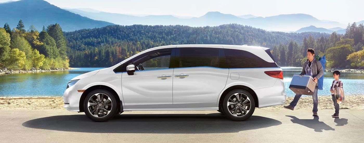 A white 2023 Honda Odyssey is shown from the side near a lake.