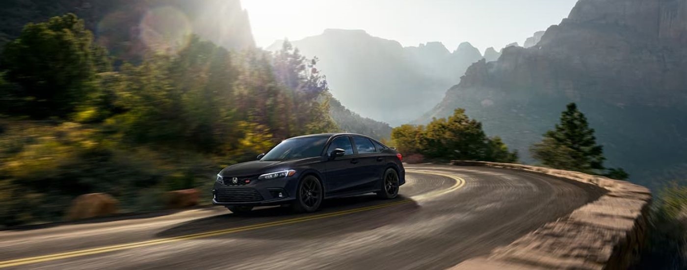 A black 2023 Honda Civic Si is shown rounding the corner on a mountain road.