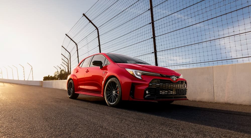 A red 2024 Toyota Corolla GR parked next to a fence.