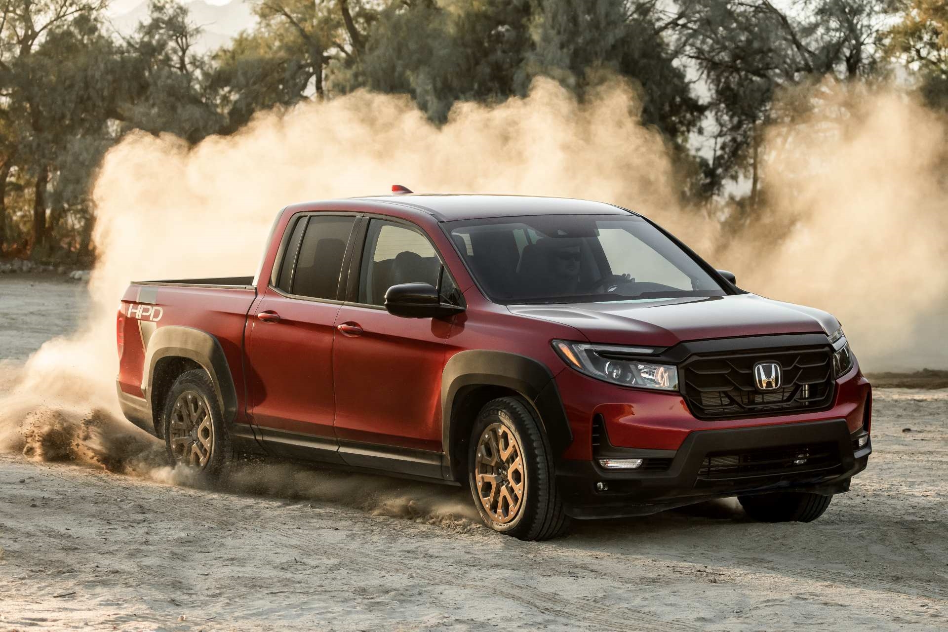 Newer used red Honda Ridgeline churning dust on sand at sunset