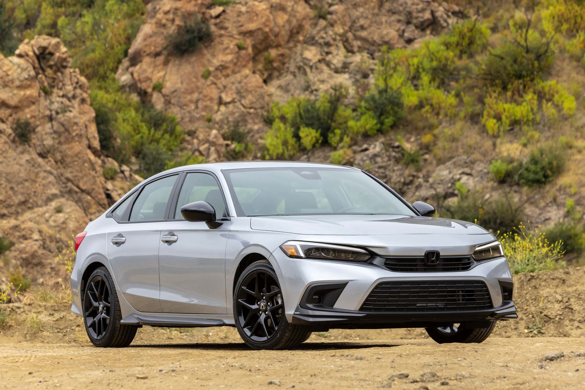 Honda Civic sitting on sand with rocky background.