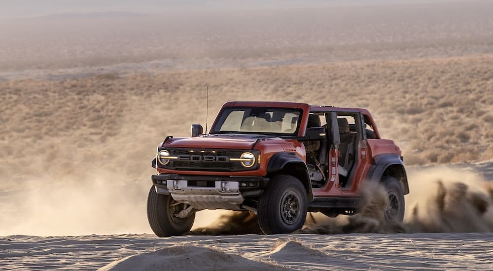 An orange 2024 Ford Bronco Raptor is shown from the front at an angle.