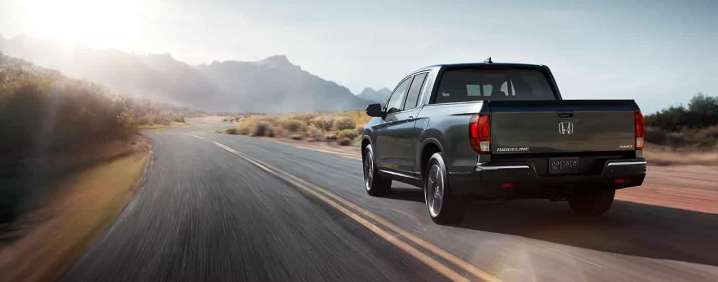 A dark grey 2020 Honda Ridgeline RTL-E is shown from the rear driving toward a mountain.