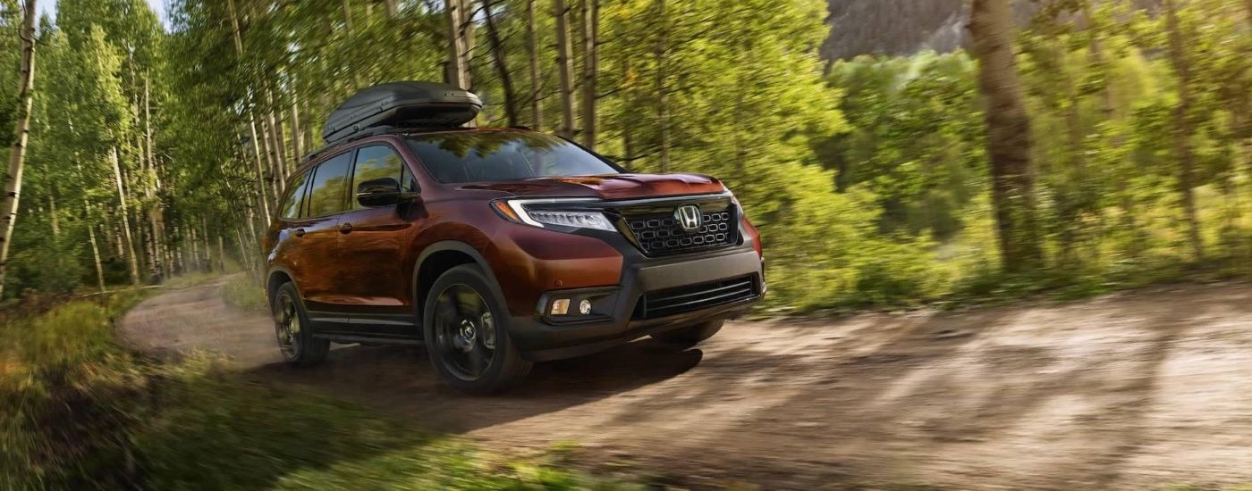 A maroon 2020 Honda Passport is shown shown driving on a tree-lined trail.