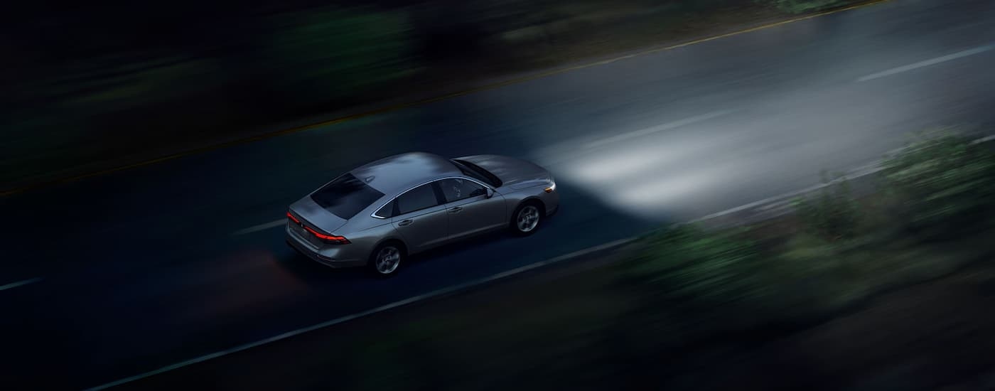 A grey 2024 Honda Accord LX is driving on a tree-lined road at night.